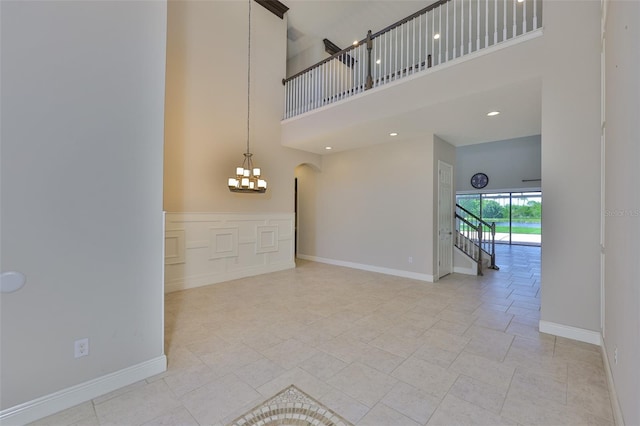 unfurnished living room featuring a chandelier, a high ceiling, baseboards, and arched walkways