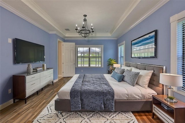 bedroom featuring wood finished floors, a chandelier, baseboards, ornamental molding, and a raised ceiling