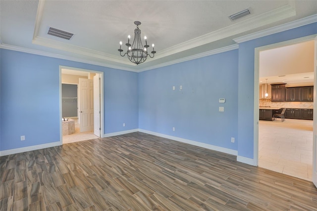 spare room featuring a chandelier, a tray ceiling, baseboards, crown molding, and wood finished floors
