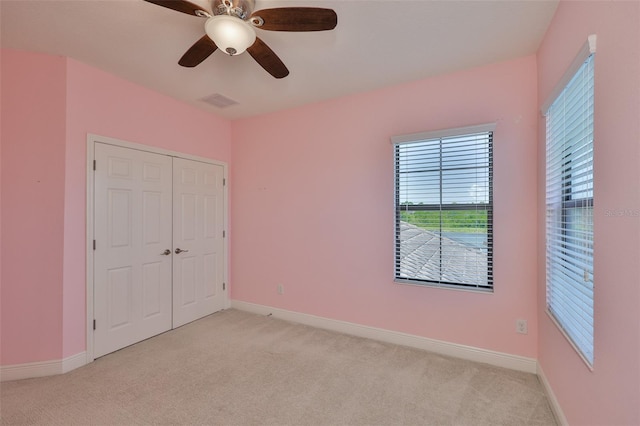unfurnished bedroom featuring light carpet, baseboards, a closet, and a ceiling fan
