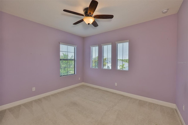 empty room featuring light colored carpet, a ceiling fan, and baseboards