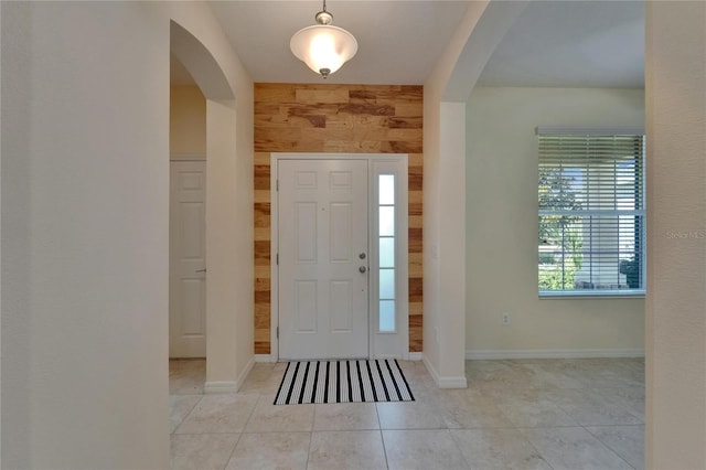tiled foyer featuring arched walkways, wooden walls, and baseboards