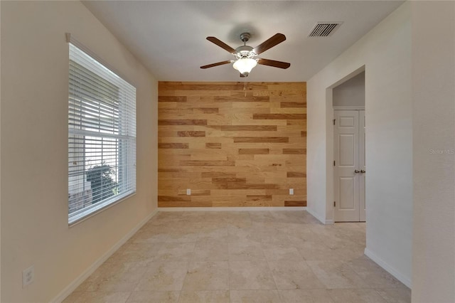 unfurnished room with wooden walls, ceiling fan, an accent wall, and baseboards