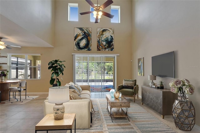 living room featuring ceiling fan, a towering ceiling, healthy amount of natural light, baseboards, and light tile patterned floors