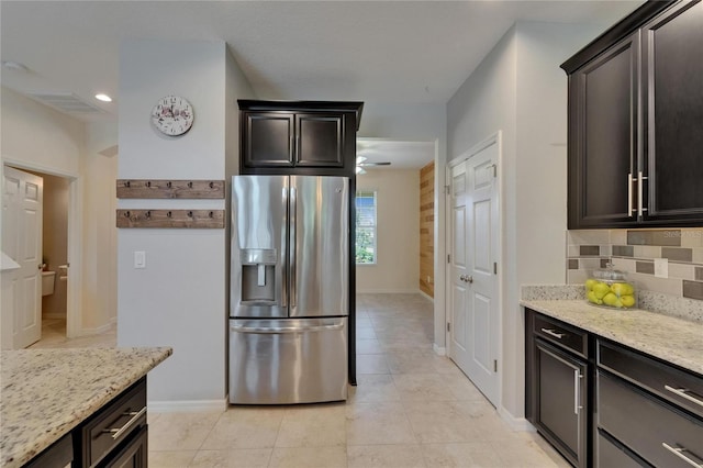 kitchen featuring stainless steel fridge, light stone countertops, backsplash, light tile patterned floors, and baseboards