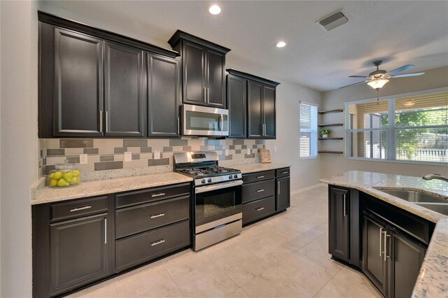 kitchen featuring stainless steel appliances, a sink, decorative backsplash, baseboards, and ceiling fan