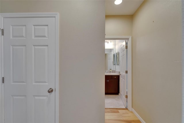 hallway with light wood-style flooring, a sink, and baseboards