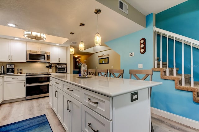 9484 Tara Cay Ct Unit 8, Seminole, FL 33776 - kitchen with appliances with stainless steel finishes, light wood finished floors, tasteful backsplash, white cabinetry, and a center island