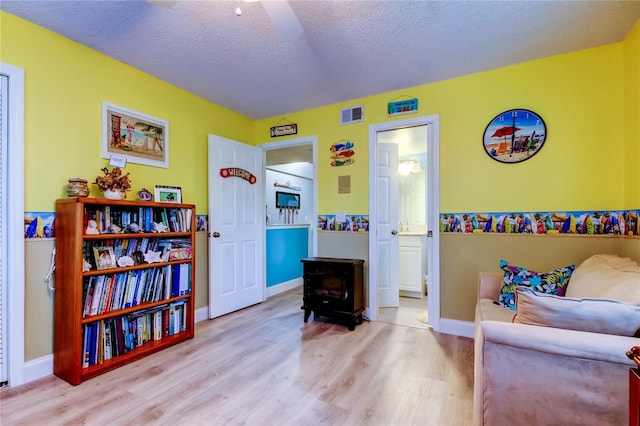 9484 Tara Cay Ct Unit 8, Seminole, FL 33776 - living area with a wood stove, wood finished floors, a textured ceiling, baseboards, and a ceiling fan