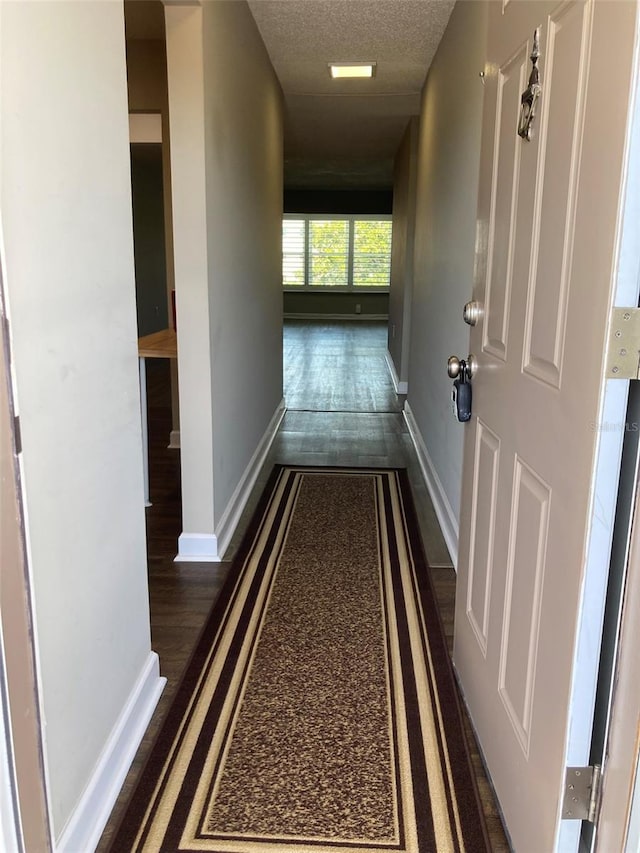 hallway with baseboards, wood finished floors, and a textured ceiling