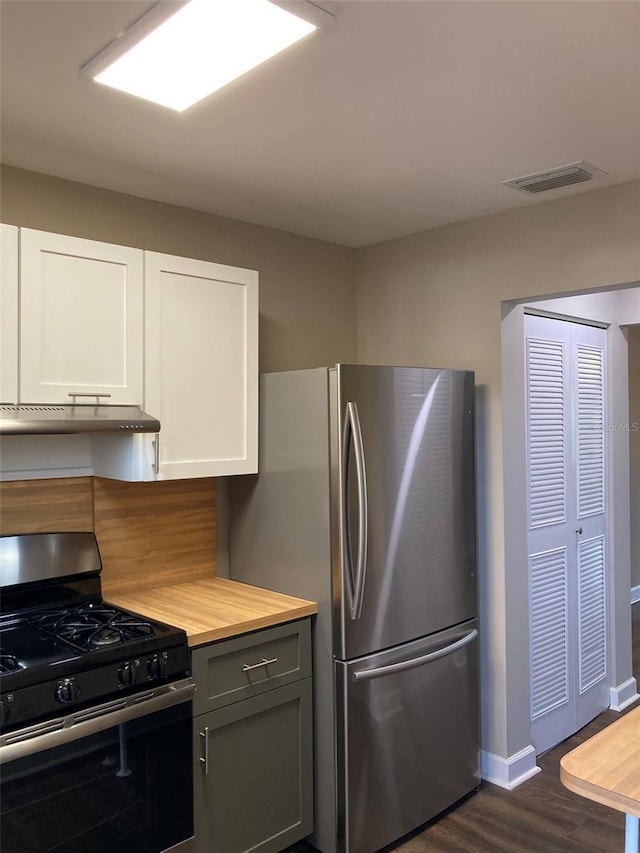 kitchen featuring gas range, under cabinet range hood, dark wood finished floors, butcher block countertops, and freestanding refrigerator