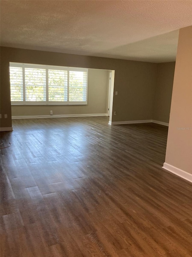 empty room featuring a textured ceiling, baseboards, and dark wood-style flooring
