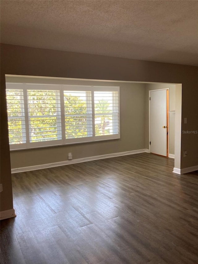 empty room with healthy amount of natural light, a textured ceiling, dark wood-style floors, and baseboards