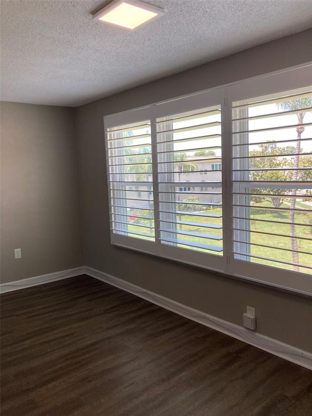 empty room with a textured ceiling, dark wood finished floors, and baseboards