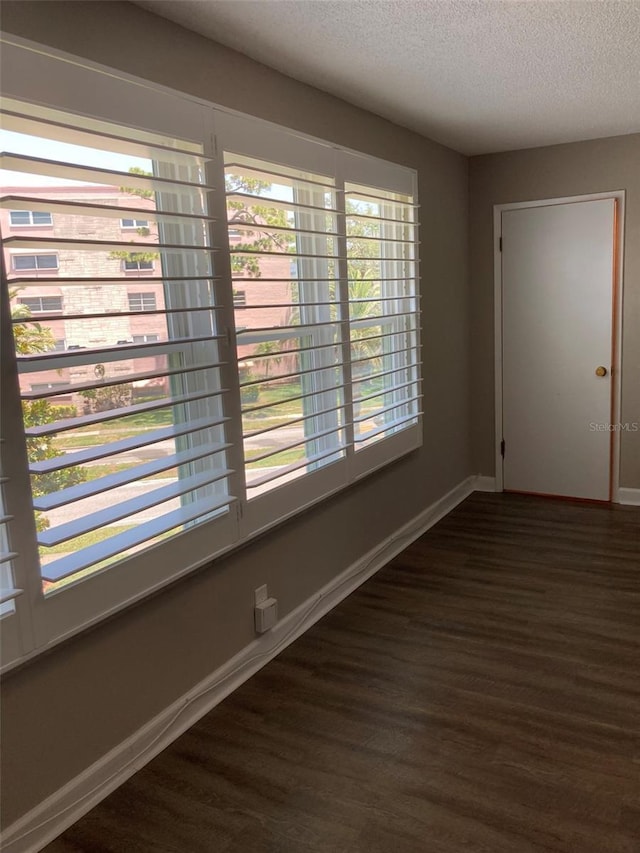 spare room with wood finished floors, a textured ceiling, and baseboards