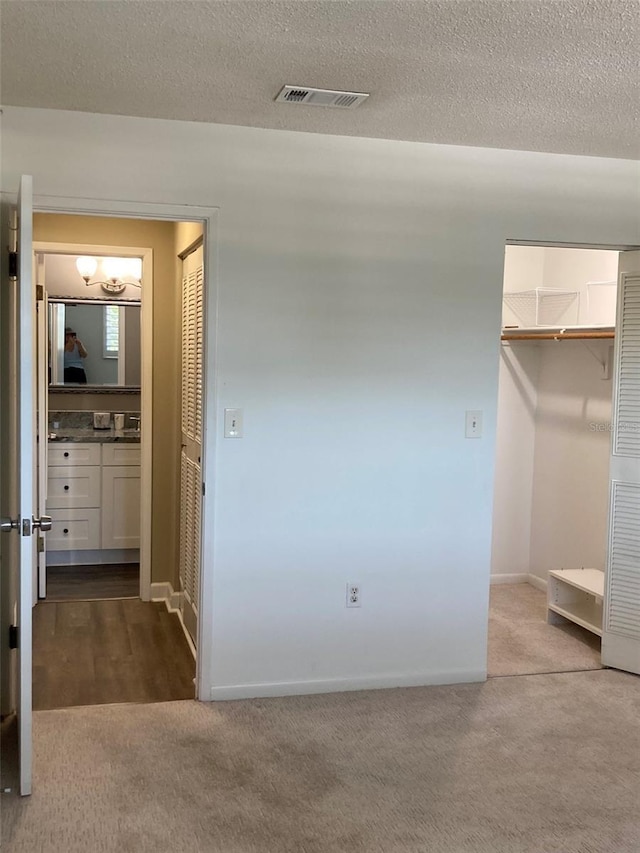 unfurnished bedroom with carpet flooring, a closet, baseboards, a walk in closet, and a textured ceiling