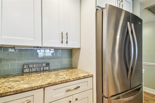 200 1st Ave Unit 309, St Pete Beach, FL 33706 - kitchen with freestanding refrigerator, tasteful backsplash, light stone counters, white cabinets, and wood finished floors