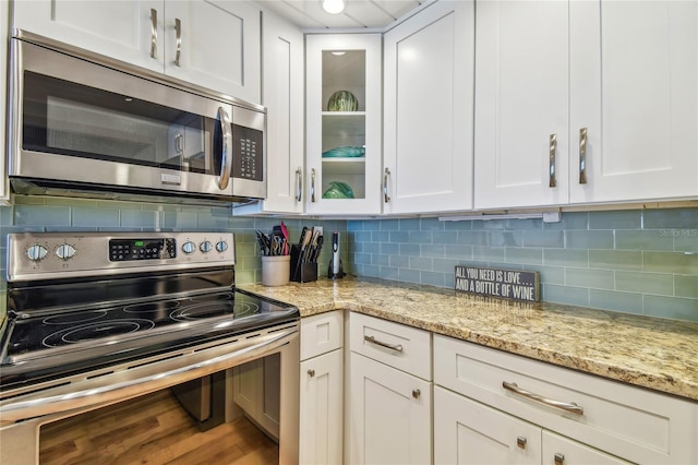 200 1st Ave Unit 309, St Pete Beach, FL 33706 - kitchen with appliances with stainless steel finishes, white cabinets, glass insert cabinets, light stone countertops, and decorative backsplash