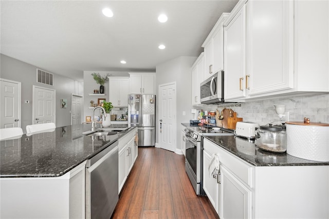 kitchen with appliances with stainless steel finishes, a sink, dark wood-type flooring, white cabinets, and tasteful backsplash