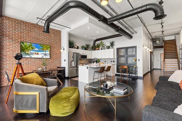 175 S 2nd St S Ph-16, Saint Petersburg, FL 33701 - living room with brick wall, a high ceiling, dark wood-style flooring, stairs, and baseboards