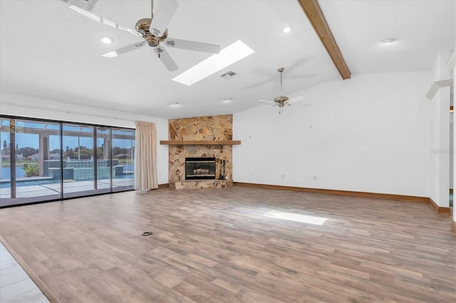 8827 Scout Lake Ct, New Port Richey, FL 34654 - unfurnished living room with a ceiling fan, a skylight, a stone fireplace, wood finished floors, and baseboards
