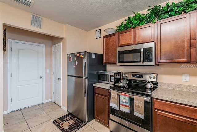 kitchen with appliances with stainless steel finishes, light countertops, light tile patterned floors, and a textured ceiling