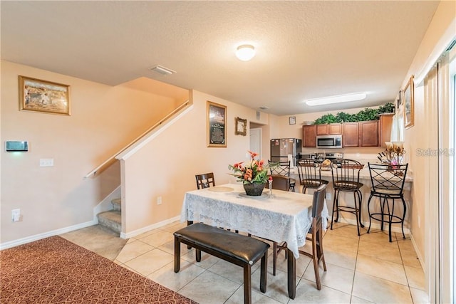 dining space with stairs, light tile patterned floors, a textured ceiling, and baseboards