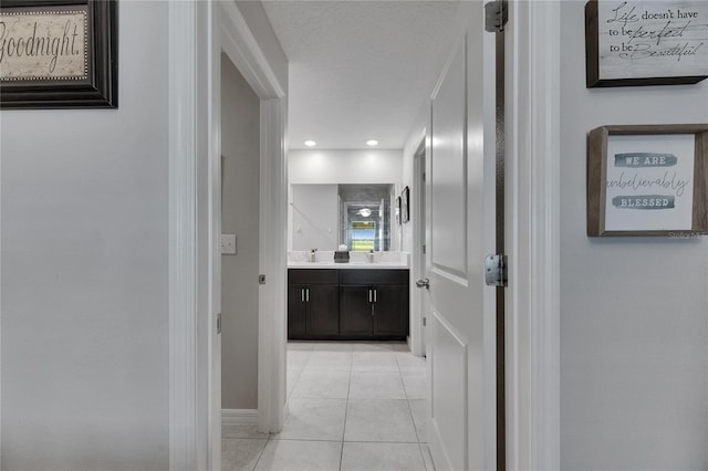 corridor with light tile patterned floors, baseboards, and a sink