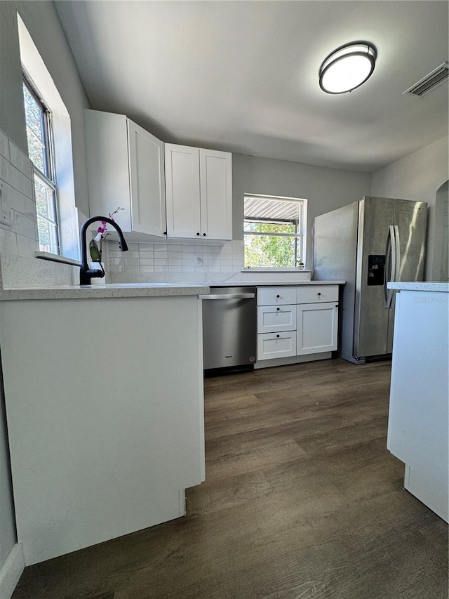 1675 13th Ave S, Saint Petersburg, FL 33712 - kitchen with stainless steel appliances, white cabinets, tasteful backsplash, dark wood-style flooring, and light countertops