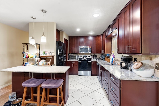 kitchen with stainless steel appliances, a sink, reddish brown cabinets, decorative backsplash, and a kitchen bar