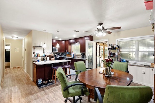 dining space featuring a ceiling fan, light wood finished floors, and baseboards