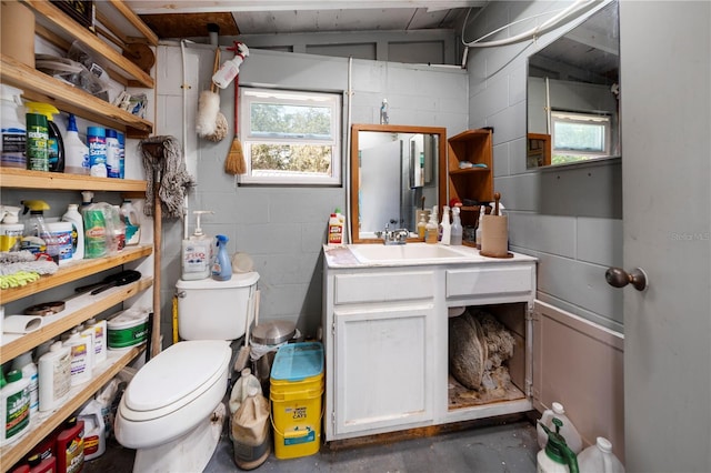 bathroom featuring concrete flooring, toilet, concrete block wall, and vanity