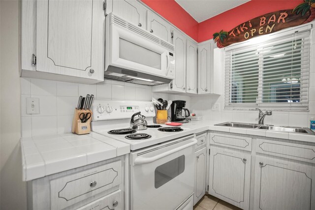 600 71st Ave Unit 18, St Pete Beach, FL 33706 - kitchen featuring white appliances, tile countertops, a sink, tasteful backsplash, and white cabinets