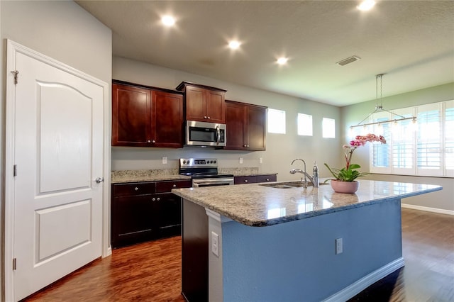 kitchen with appliances with stainless steel finishes, a sink, dark wood-style floors, a kitchen island with sink, and light stone countertops