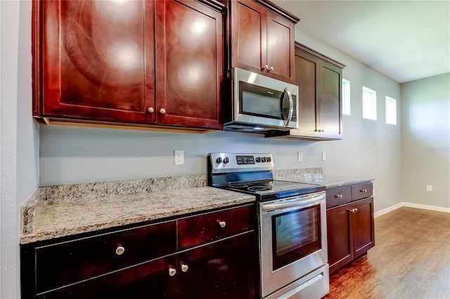 kitchen featuring appliances with stainless steel finishes, dark brown cabinets, wood finished floors, baseboards, and light stone countertops
