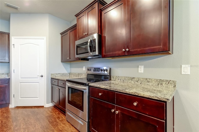 kitchen featuring stainless steel appliances, wood finished floors, dark brown cabinets, and light stone countertops