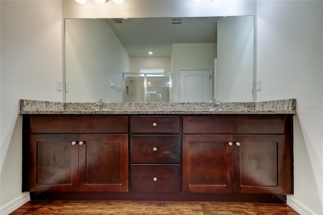 full bath featuring a stall shower, baseboards, double vanity, and wood finished floors