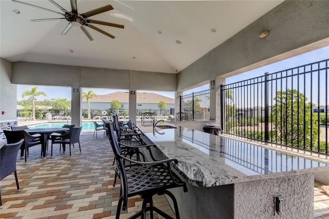 view of patio featuring ceiling fan, fence, a community pool, and exterior bar