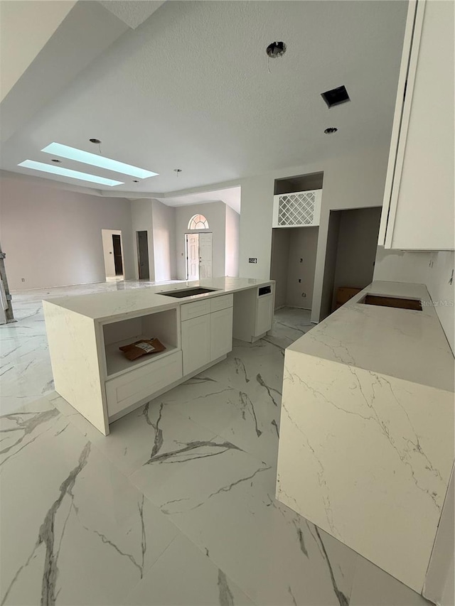 14273 Nugent Cir, Spring Hill, FL 34609 - kitchen with a skylight, white cabinets, light marble finish floors, light stone counters, and a textured ceiling