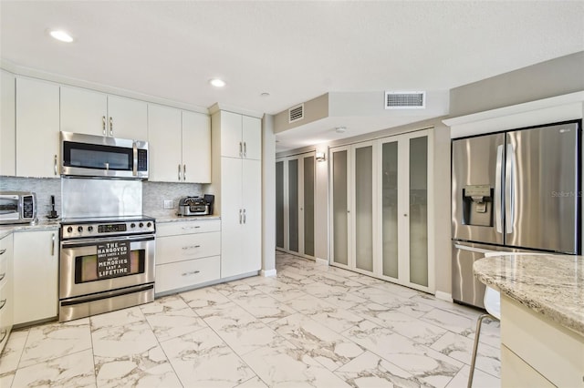 kitchen with appliances with stainless steel finishes, light marble finish floors, backsplash, white cabinets, and recessed lighting