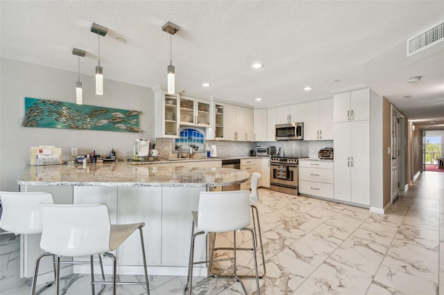 kitchen featuring stainless steel appliances, a peninsula, light marble finish floors, glass insert cabinets, and decorative light fixtures