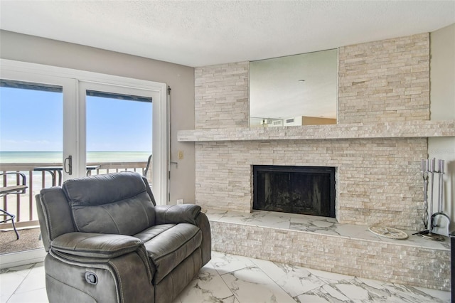 living room featuring marble finish flooring, view of water and beach, a textured ceiling, and a large fireplace
