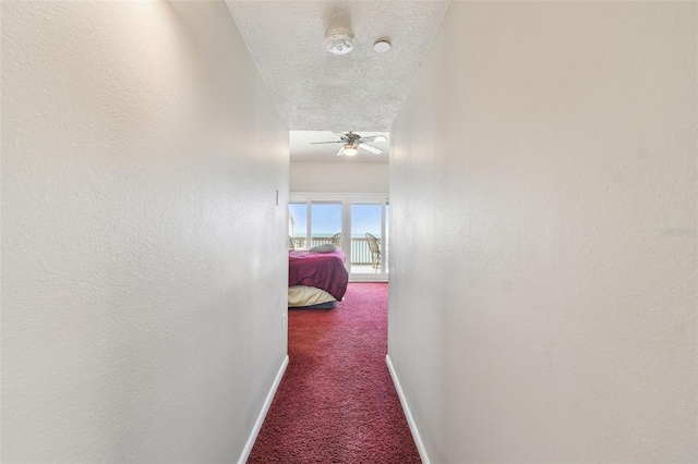 hall featuring carpet, baseboards, and a textured ceiling