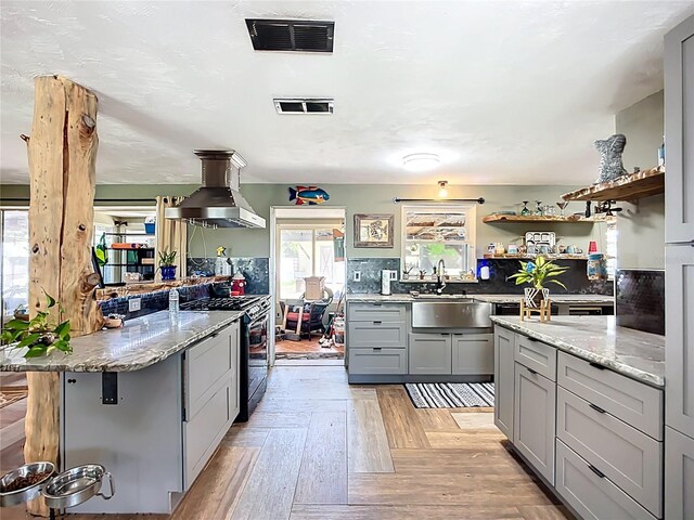 2912 Case Ave, Bradenton, FL 34207 - kitchen featuring black range with gas cooktop, gray cabinetry, ventilation hood, open shelves, and light stone counters