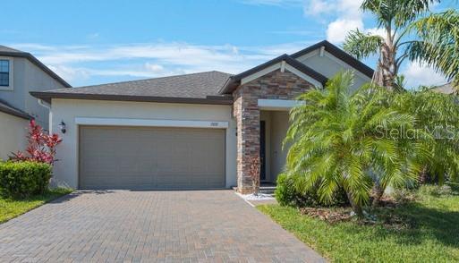 view of front facade featuring decorative driveway, an attached garage, stone siding, and stucco siding