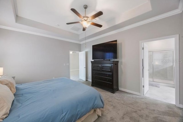 carpeted bedroom featuring a tray ceiling, ornamental molding, baseboards, ensuite bath, and a ceiling fan