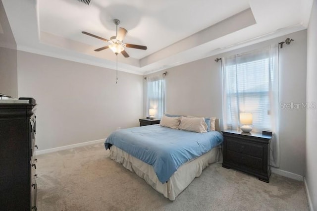 bedroom with a tray ceiling, light colored carpet, baseboards, and ceiling fan