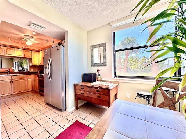 kitchen with appliances with stainless steel finishes, a sink, light tile patterned floors, healthy amount of natural light, and a textured ceiling