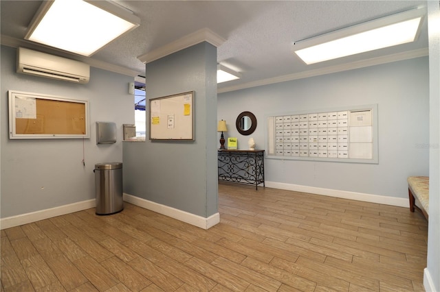 unfurnished room with an AC wall unit, mail area, ornamental molding, light wood-style flooring, and a textured ceiling