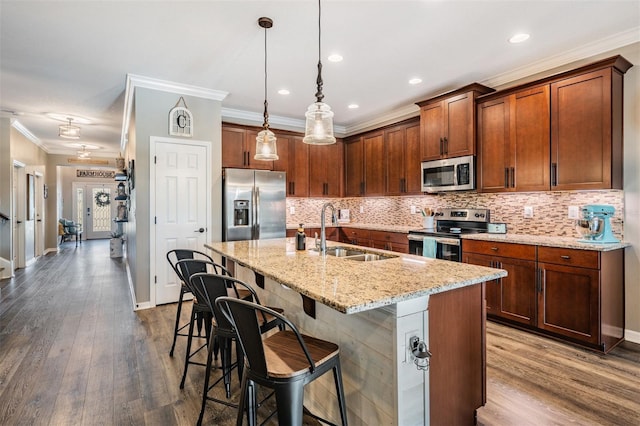 kitchen with appliances with stainless steel finishes, a sink, crown molding, a center island with sink, and a kitchen bar